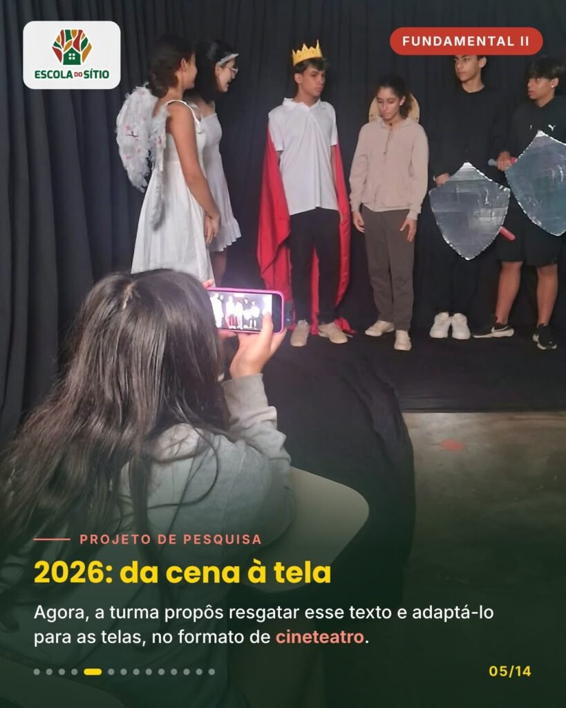 Estudante filma com o celular o elenco caracterizado em frente ao fundo preto
